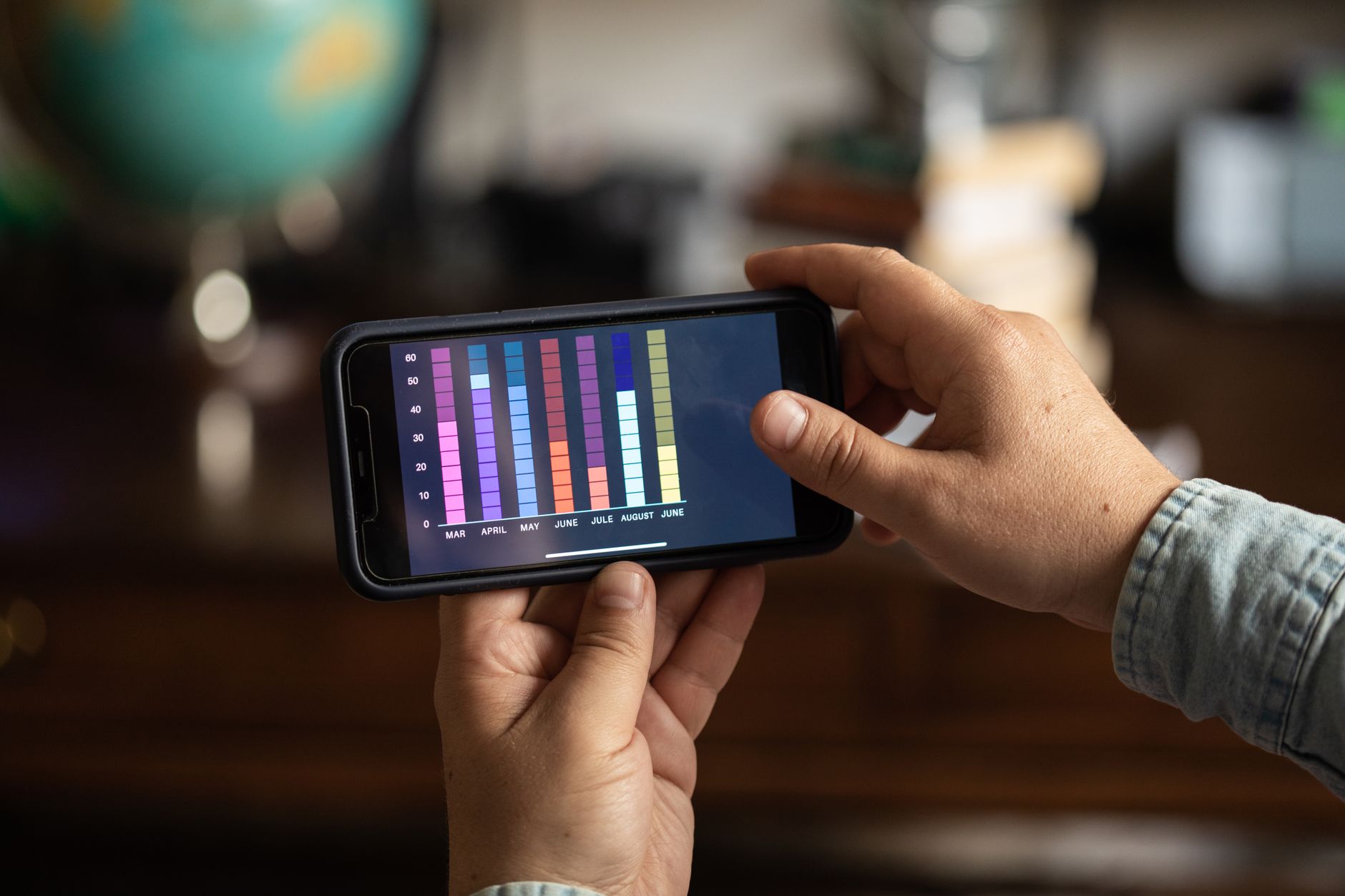 Primer plano de unas manos sosteniendo un smartphone con un gráfico de barras de colores en la pantalla.