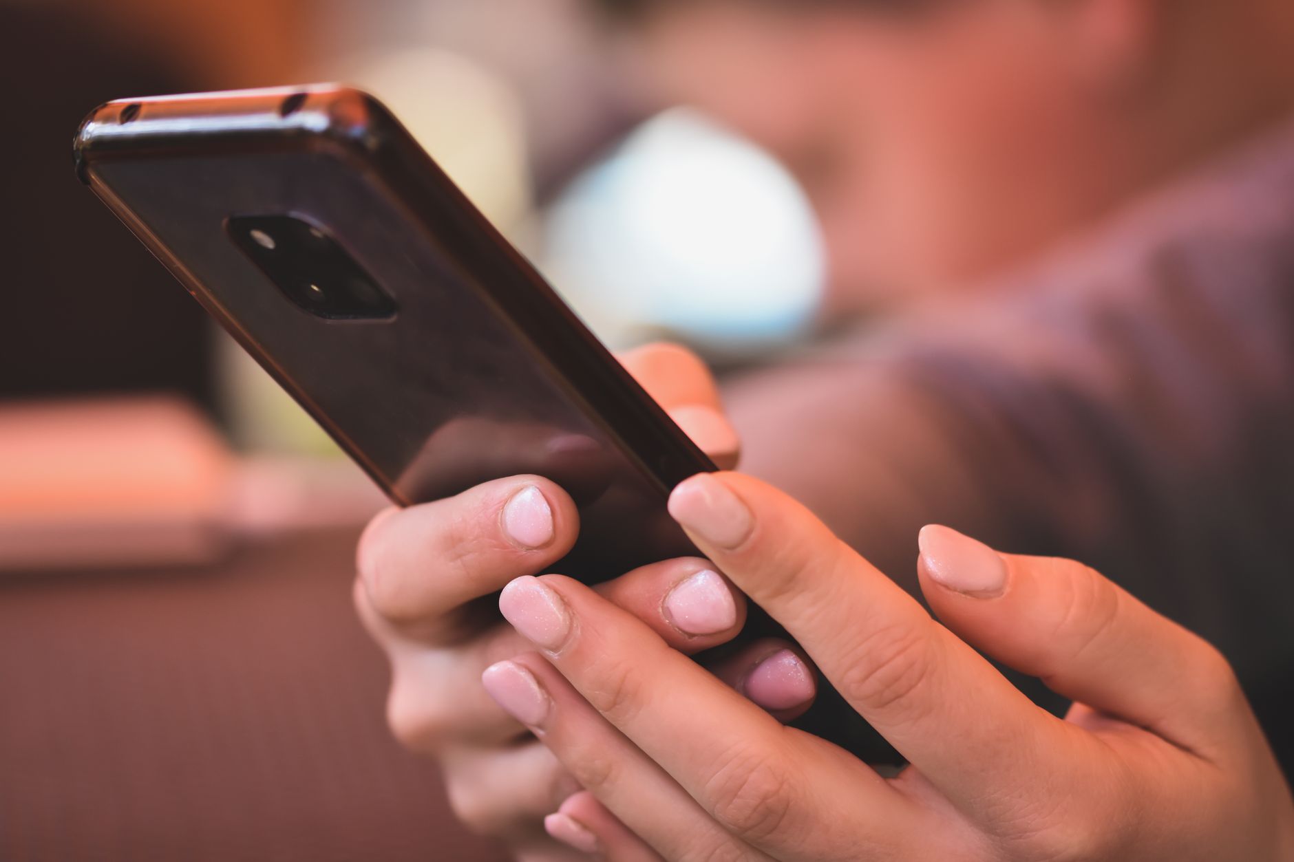 Plano cercano de unas manos con las uñas cuidadas sosteniendo un smartphone en un espacio interior.
